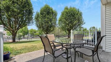 Un patio al aire libre con una mesa redonda y cuatro sillas, rodeado de árboles y vistas a un parque.
