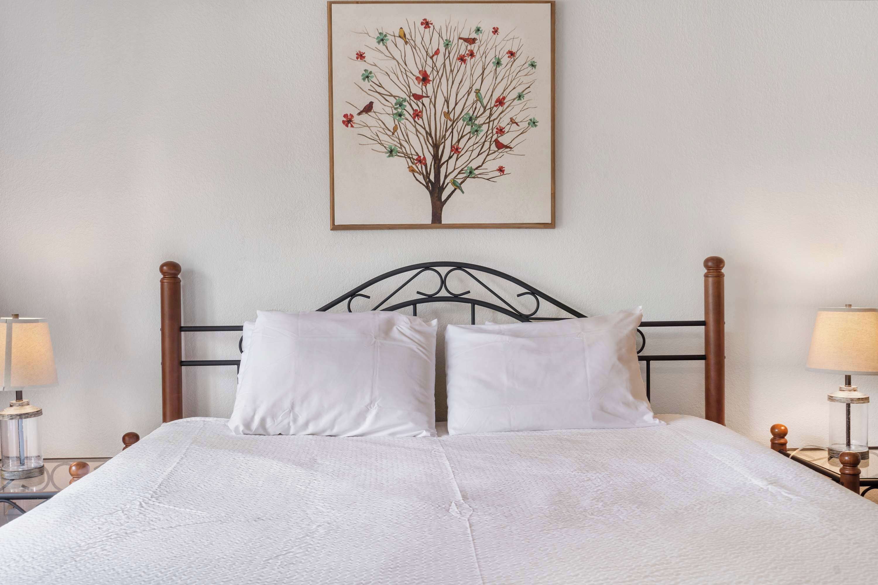A neatly made bed with white linens, a wooden headboard, and two bedside lamps.