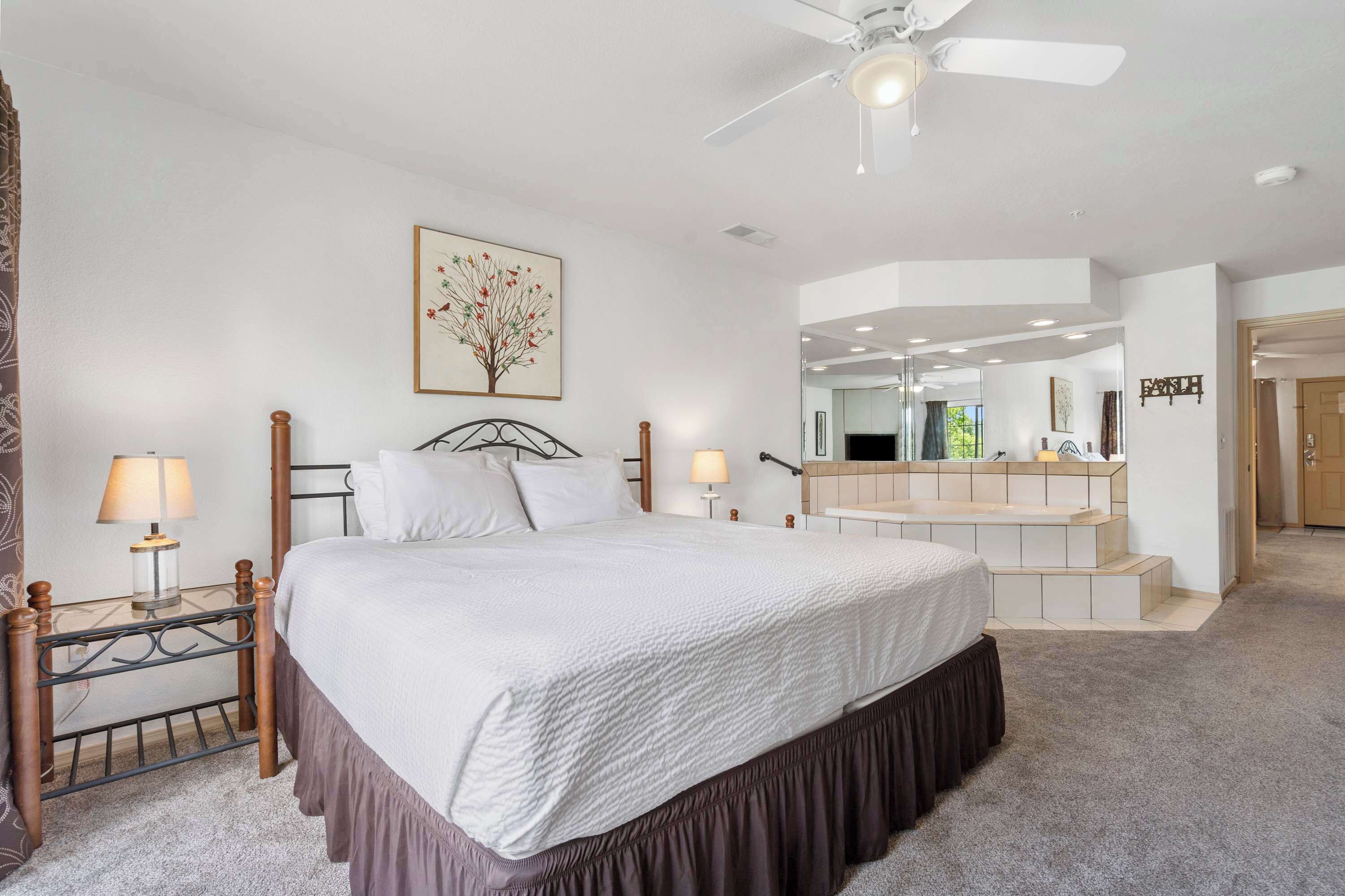 A bedroom with a large bed, bedside lamps, a ceiling fan, a mirror, and a staircase leading to an upper level.