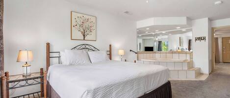 A bedroom with a large bed, bedside lamps, a ceiling fan, a mirror, and a staircase leading to an upper level.