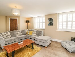 Una sala de estar con un sofá modular, una mesa de centro, una lámpara de pie y un cuadro en la pared.