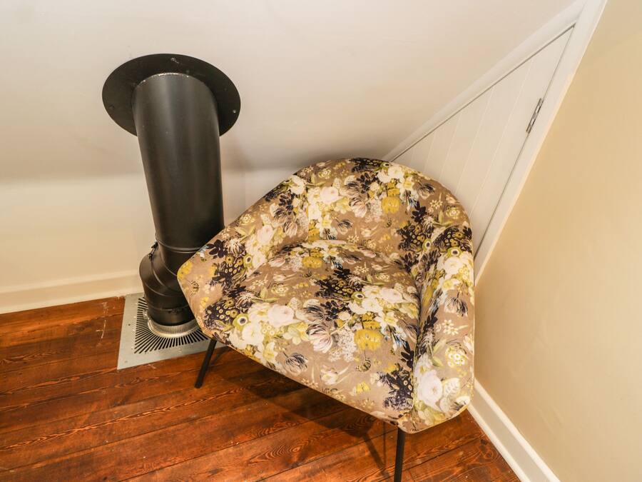 Habitación de esquina con suelo de madera, un radiador y una silla estampada con motivos florales.