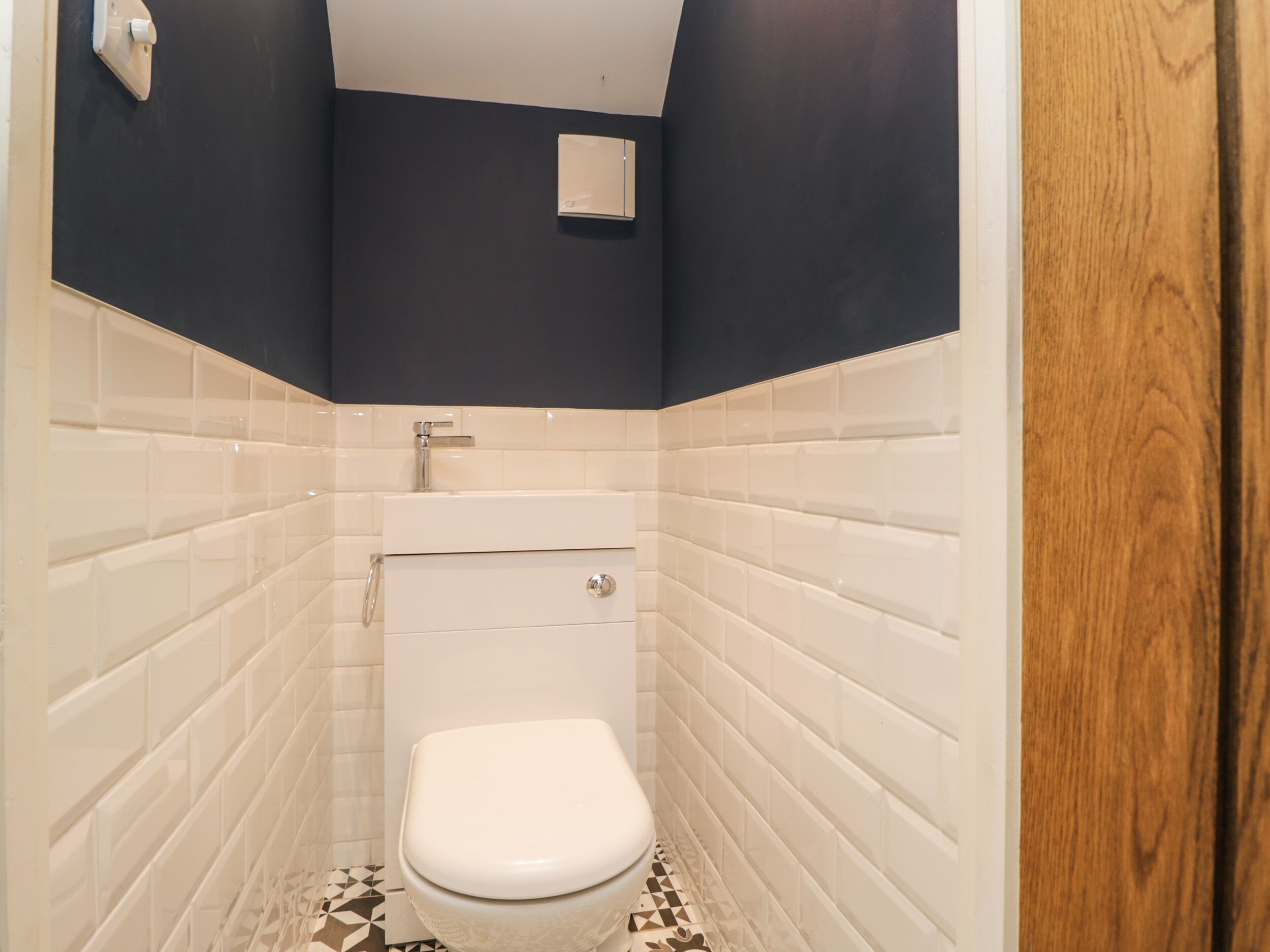 A small, narrow bathroom with white tiles, a white toilet, and a wooden door.