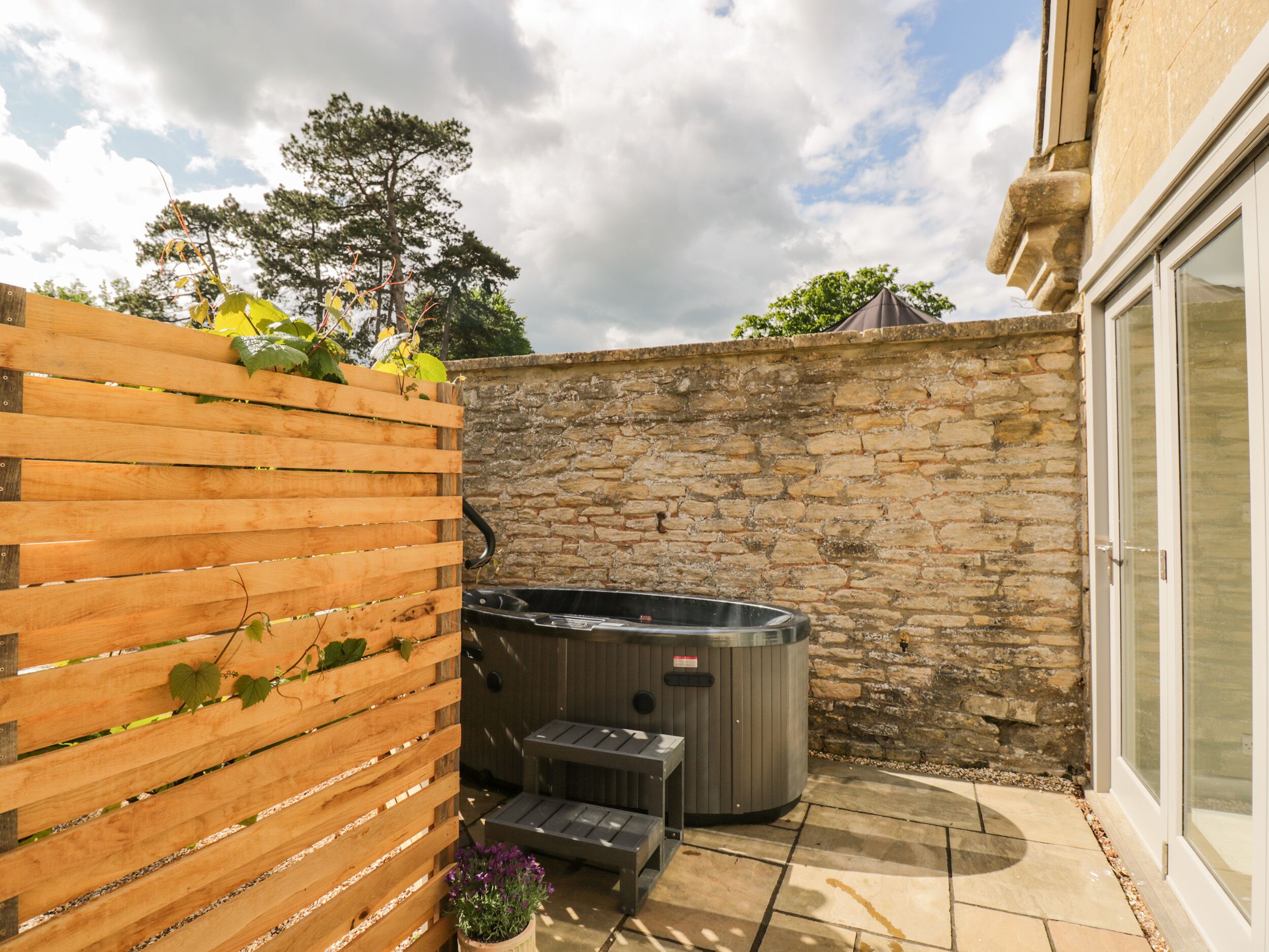 A patio area with a stone wall, a wooden fence, a hot tub, and a bench.