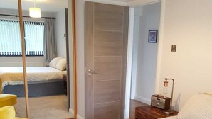 A bedroom with a bed, a chair, a bedside table, and a door leading to another room.