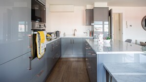 A modern kitchen with grey cabinets, stainless steel appliances, and a marble countertop.
