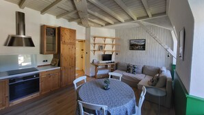 Un salon confortable avec une table à manger, un canapé et un téléviseur. La cuisine est équipée de meubles en bois et d’une cuisinière.