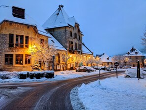 A snow-covered street with buildings, including a stone building with a sign reading "Ecole Communale". - Nid douillet 2ou4 p à St Pierre de Chartreuse (Saint-Pierre-de-Chartreuse)