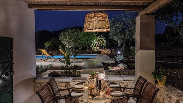 An outdoor dining area with a table set for four, surrounded by stone walls and a view of a swimming pool at night. - Trullo Orto dei Nonni - Le Case di Valentina (Ceglie Messapica)