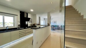 A modern kitchen with a central island, a dining area with a sofa, and a staircase leading to another level. - ALBUFEIRA DELUXE RESIDENCE WITH POOL by HOMING (Albufeira)