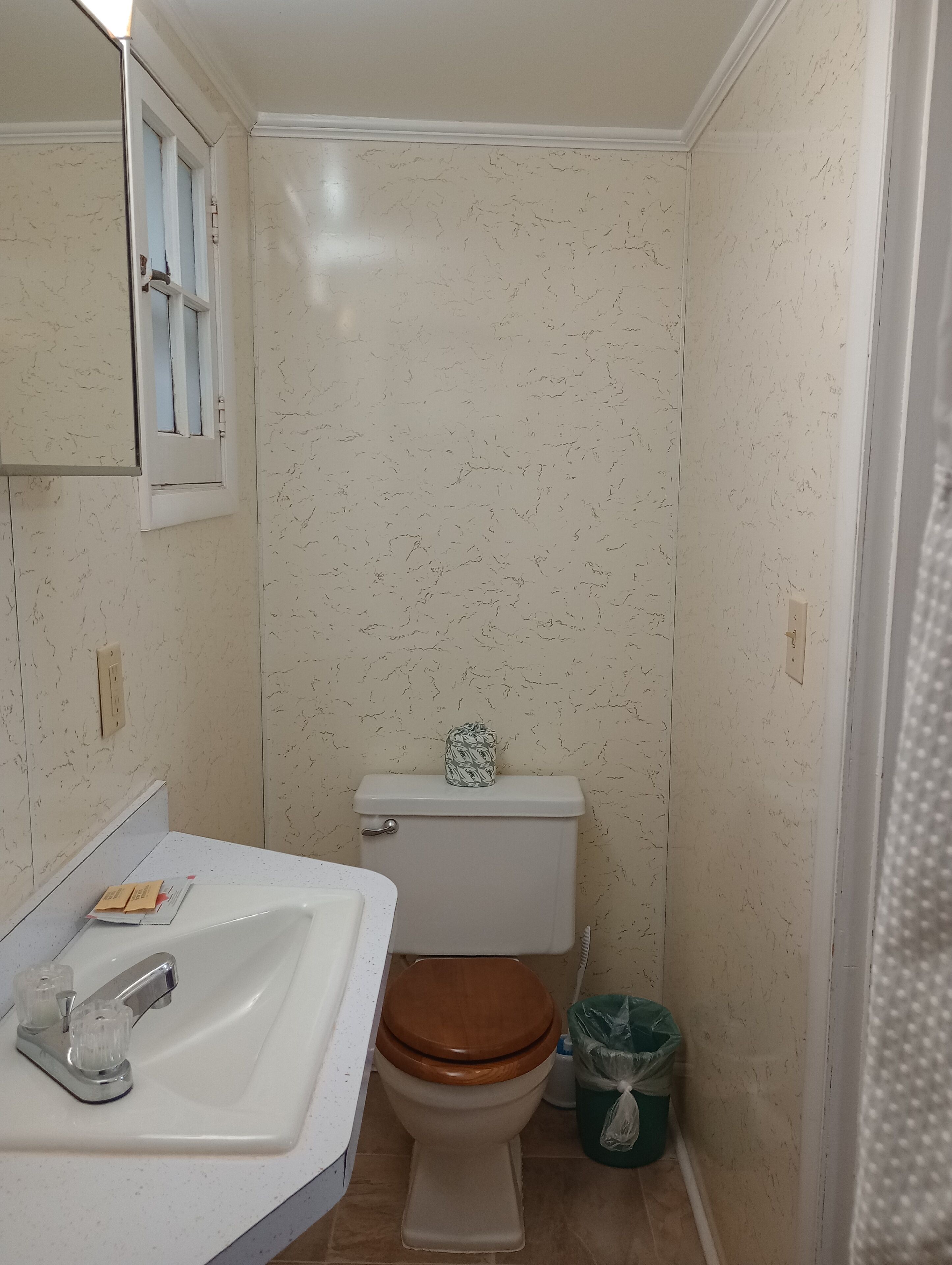 Un baño pequeño con un lavamanos blanco, un inodoro de madera y un cubo de basura verde.