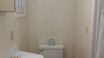 Un baño pequeño con un lavamanos blanco, un inodoro de madera y un cubo de basura verde.