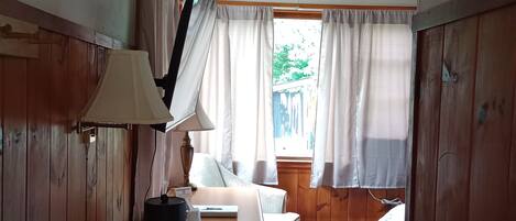 Una habitación con escritorio de madera, lámpara, papelera, cama y ventana con cortinas.