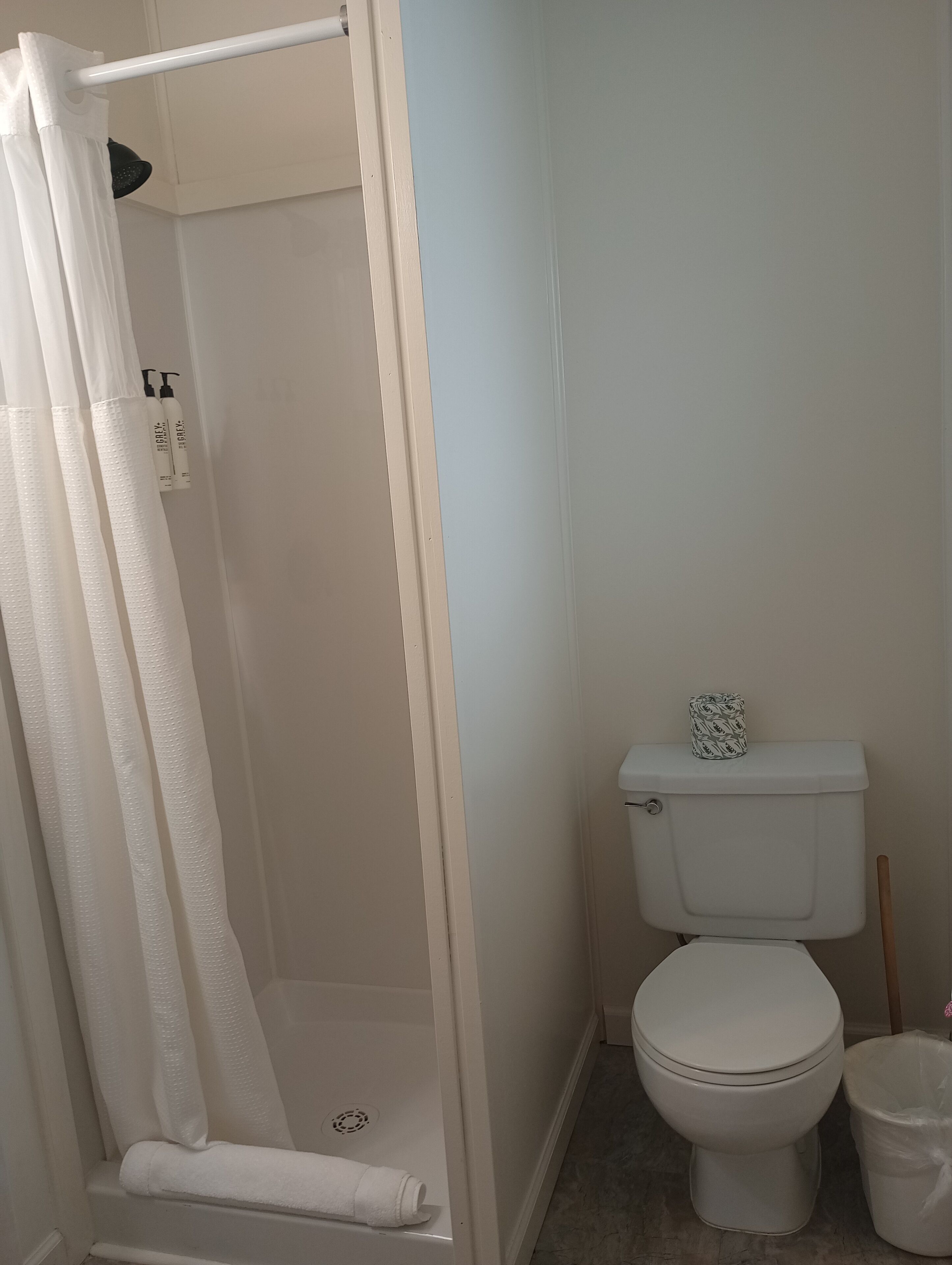 A bathroom with a shower, toilet, and a trash bin.