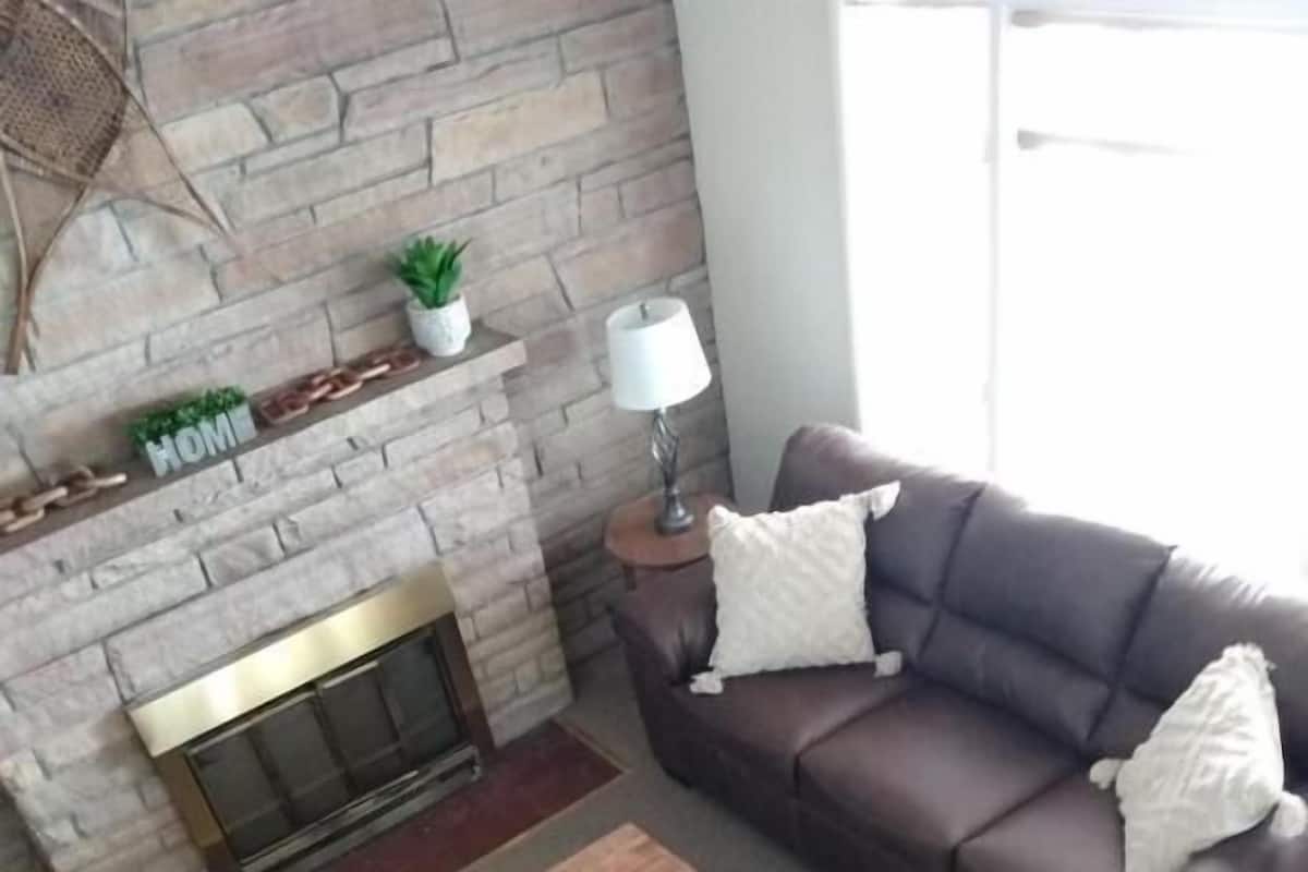 A living room with a stone fireplace, a brown leather sofa, a wooden coffee table, and a lamp on a side table.