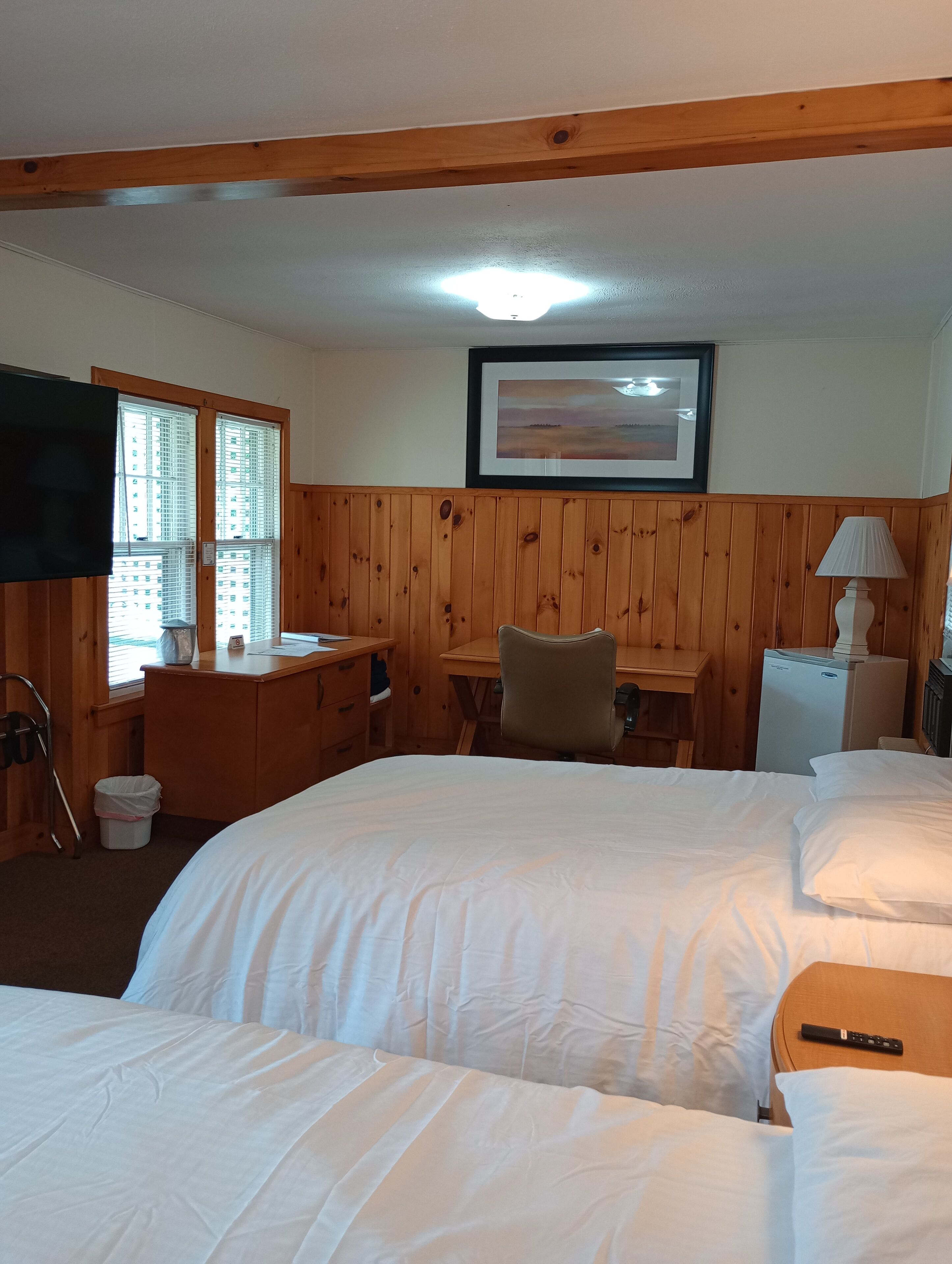 A hotel room with two beds, a desk, a chair, a television, and a framed picture on the wall.
