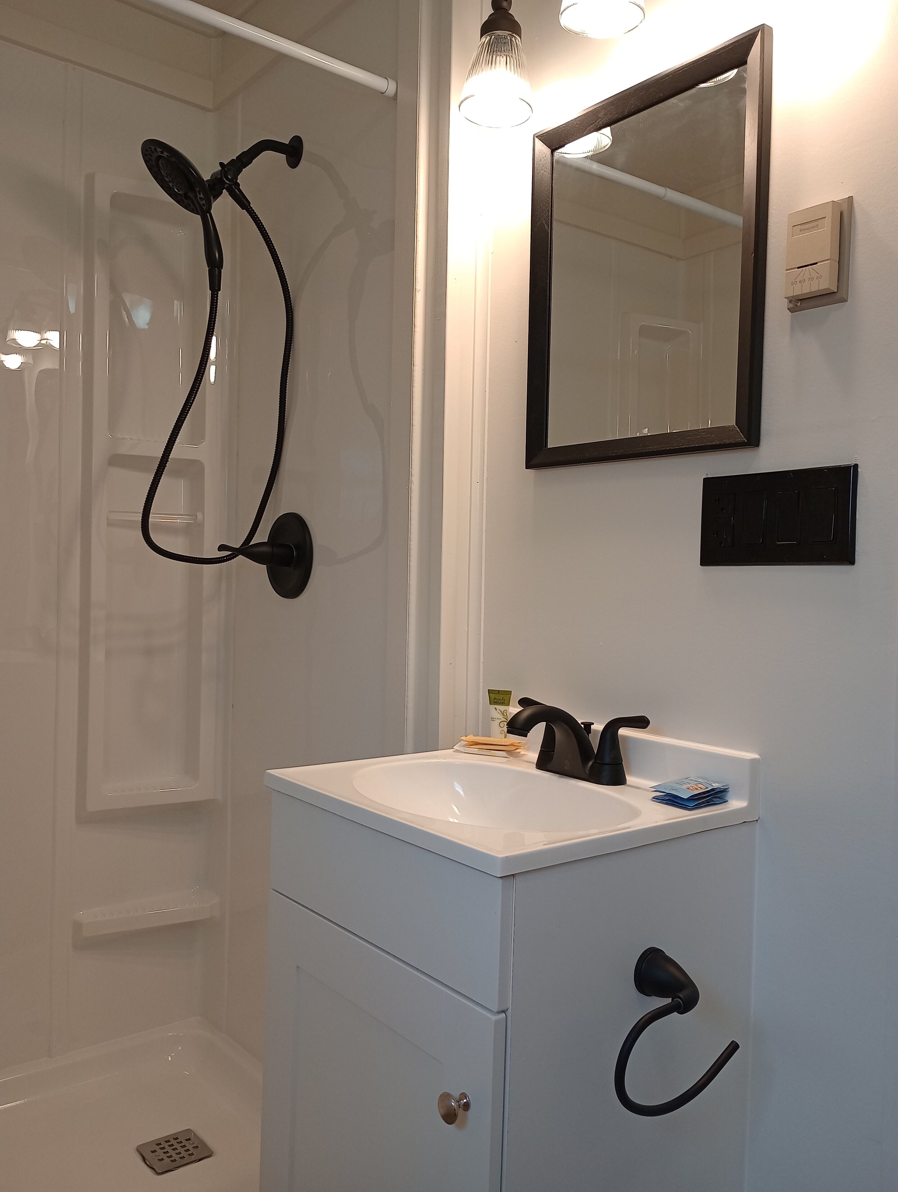 Un baño con lavamanos blanco, grifo negro y ducha con manguera negra.