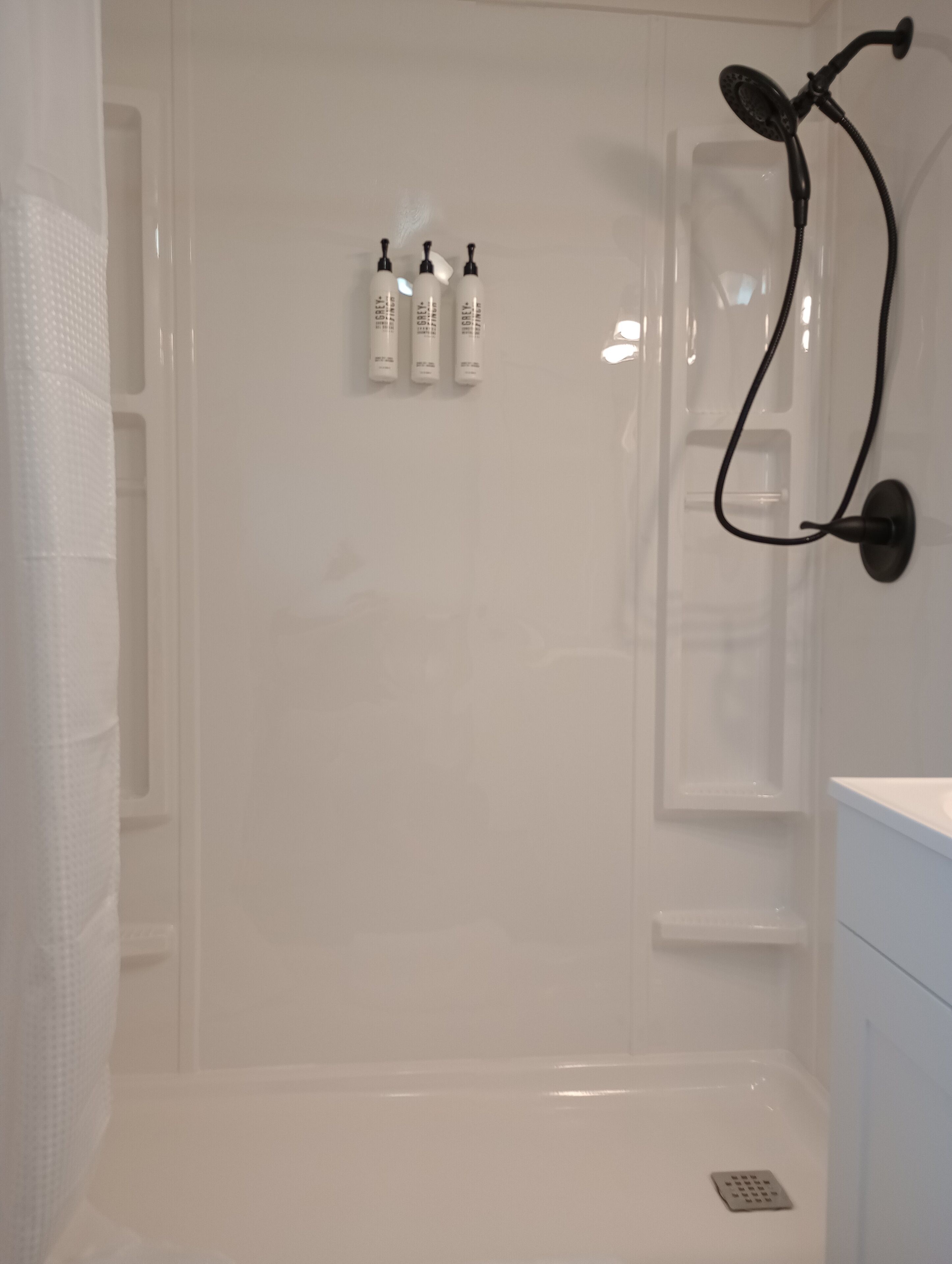 A modern shower area with a glass door, a handheld showerhead, and three bottles of shampoo on the wall.