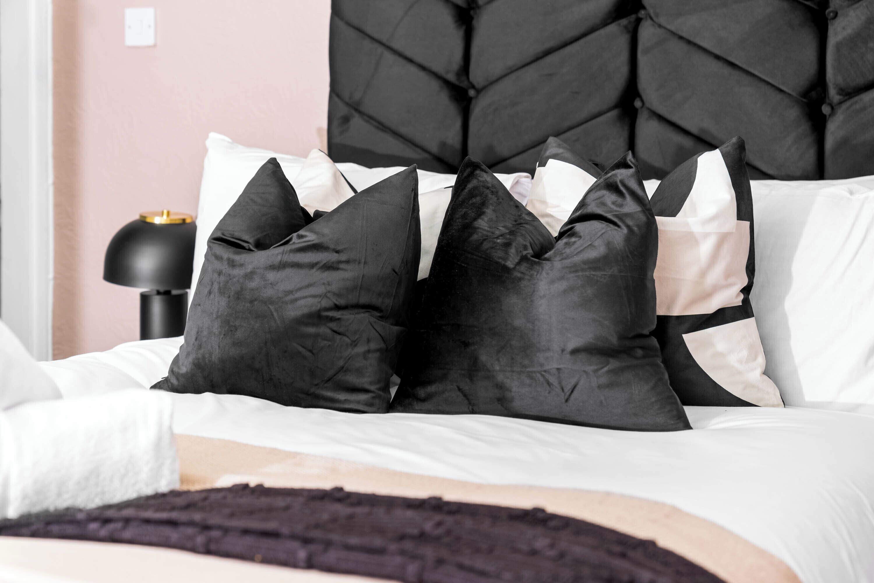 A bed with a black headboard, white and black pillows, and a black lamp on a bedside table.