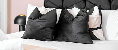 A bed with a black headboard, white and black pillows, and a black lamp on a bedside table.