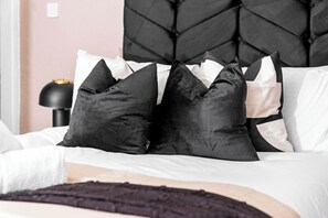 Un lit avec une tête de lit noire, des oreillers blancs et noirs, et une lampe noire posée sur une table de chevet.