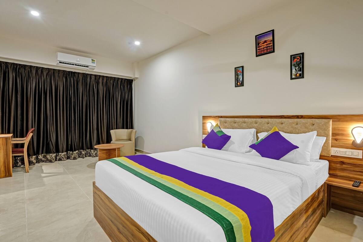 Quarto de hotel com cama, escrivaninha, cadeira e ar condicionado.