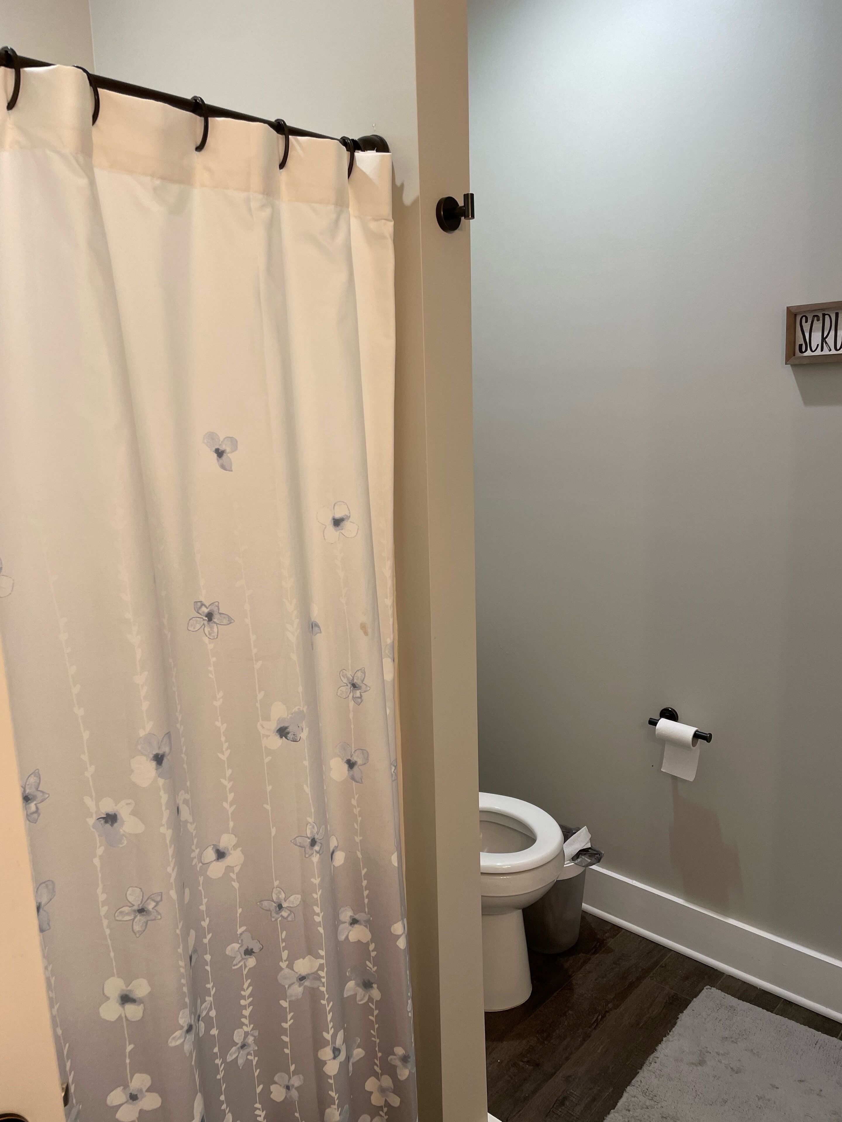 Et badeværelse med toilet, toiletpapir og et blomstret bruseforhæng.