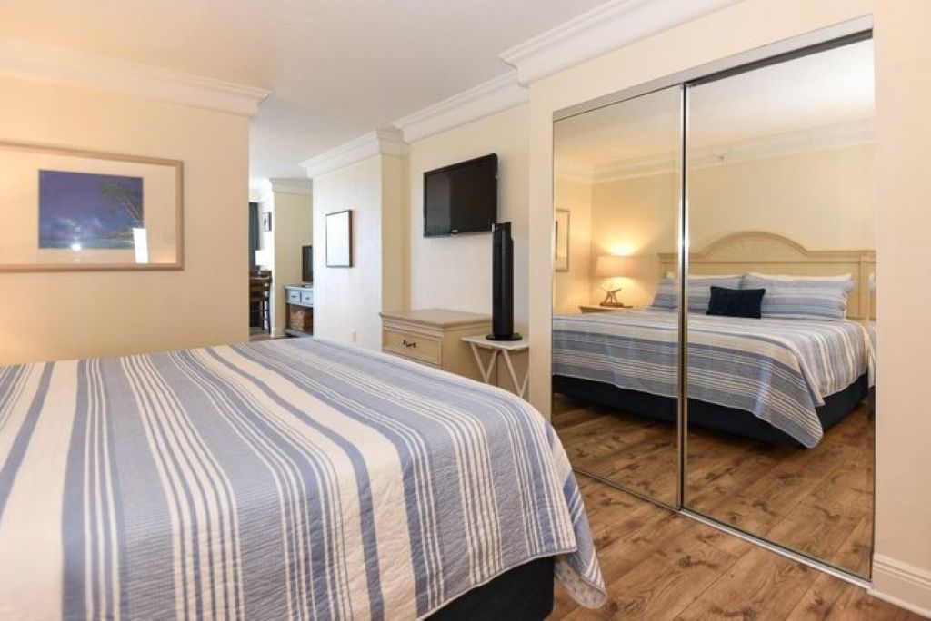Habitación de hotel con una cama grande, un televisor montado en la pared y un espejo que refleja el cuarto.