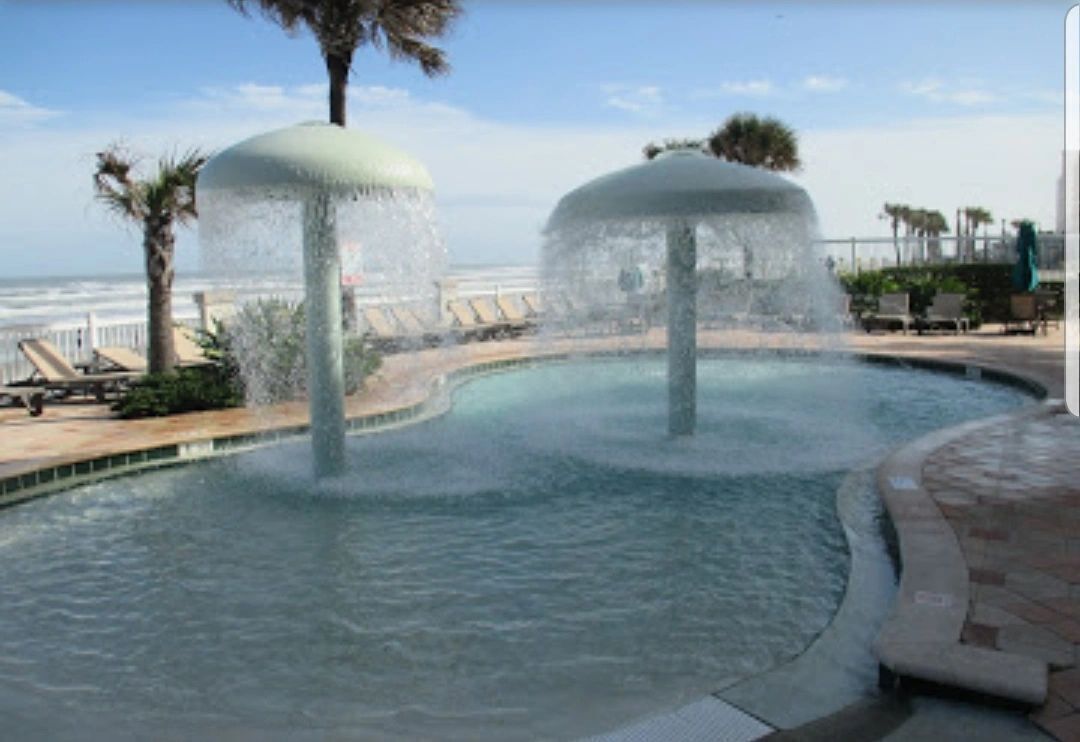 A pool with water jets, palm trees, and a view of the ocean.