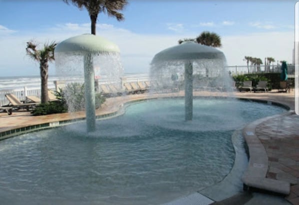 A pool with water jets, palm trees, and a view of the ocean.