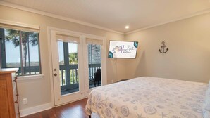 A bedroom with a large bed, a TV mounted on the wall, and a view of the outdoors through a sliding door. - Lovely Long Term Rental~ Marsh Nest (Folly Beach)