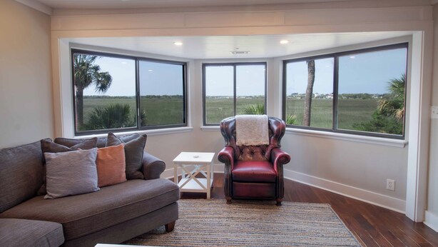 A living room with a large window, a leather armchair, and a grey sofa. - Lovely Long Term Rental~ Marsh Nest (Folly Beach)