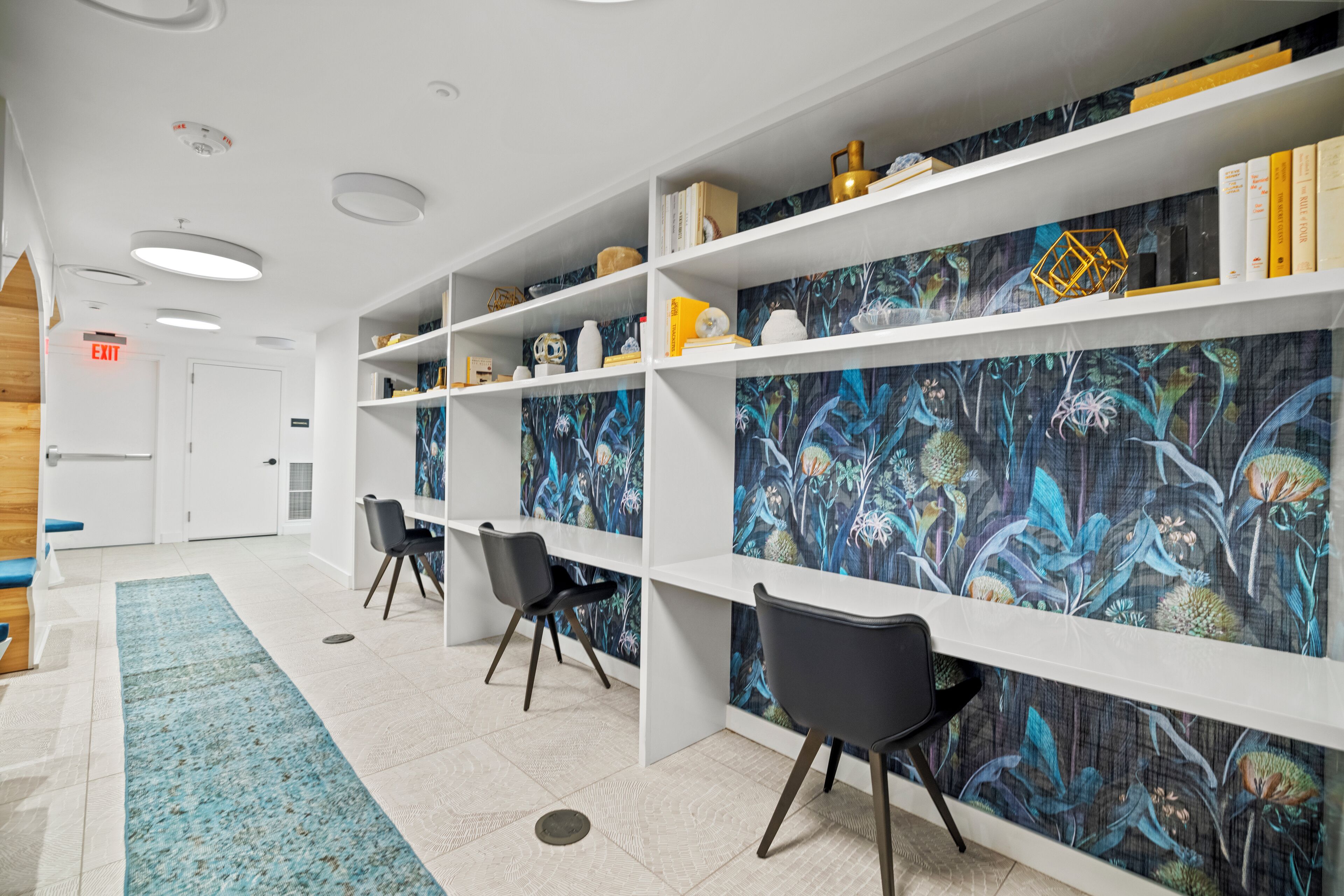 A hallway with white shelving units, black chairs, and a blue patterned carpet.