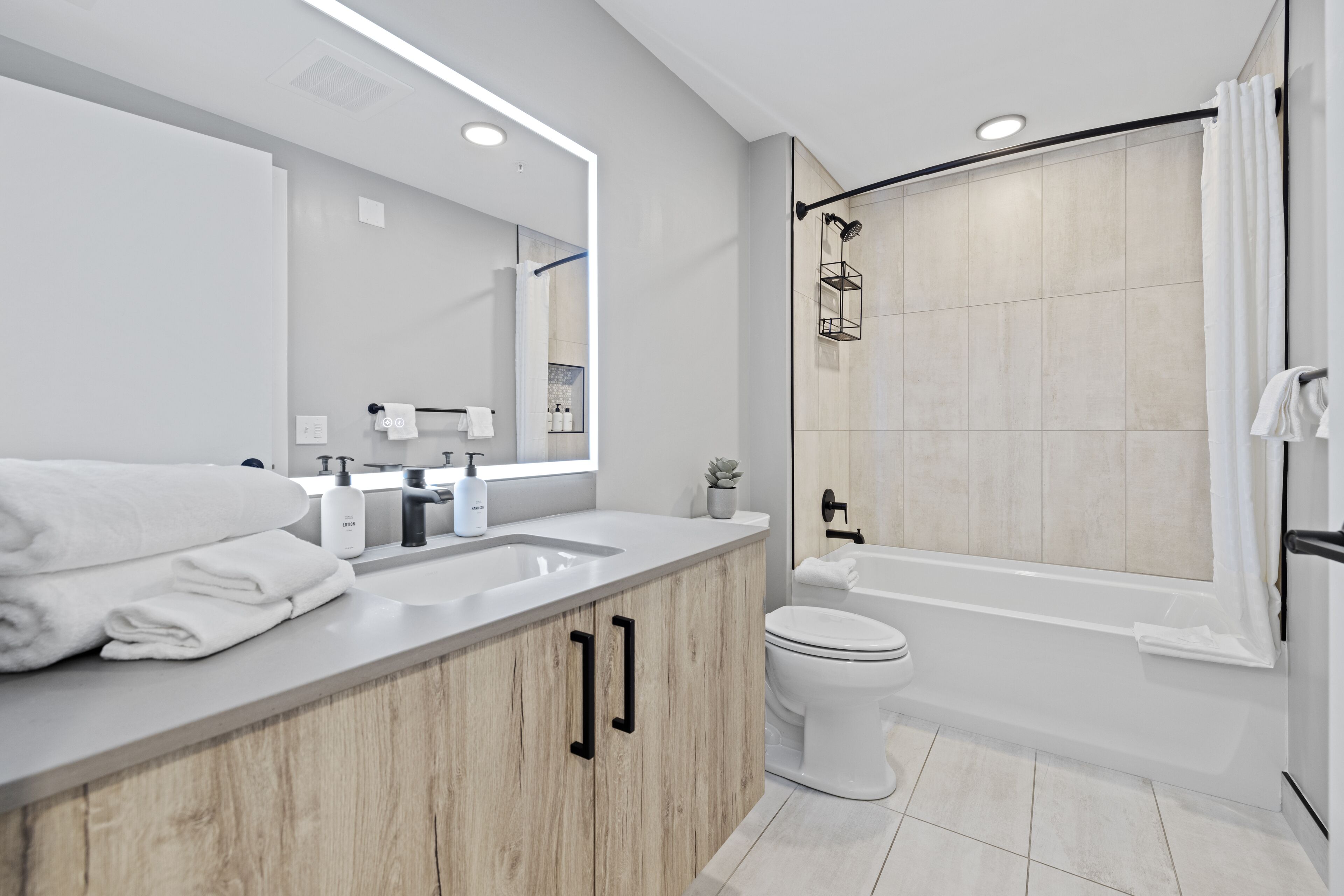 Un baño moderno con tocador de madera, un espejo grande, un lavabo blanco, inodoro y bañera.