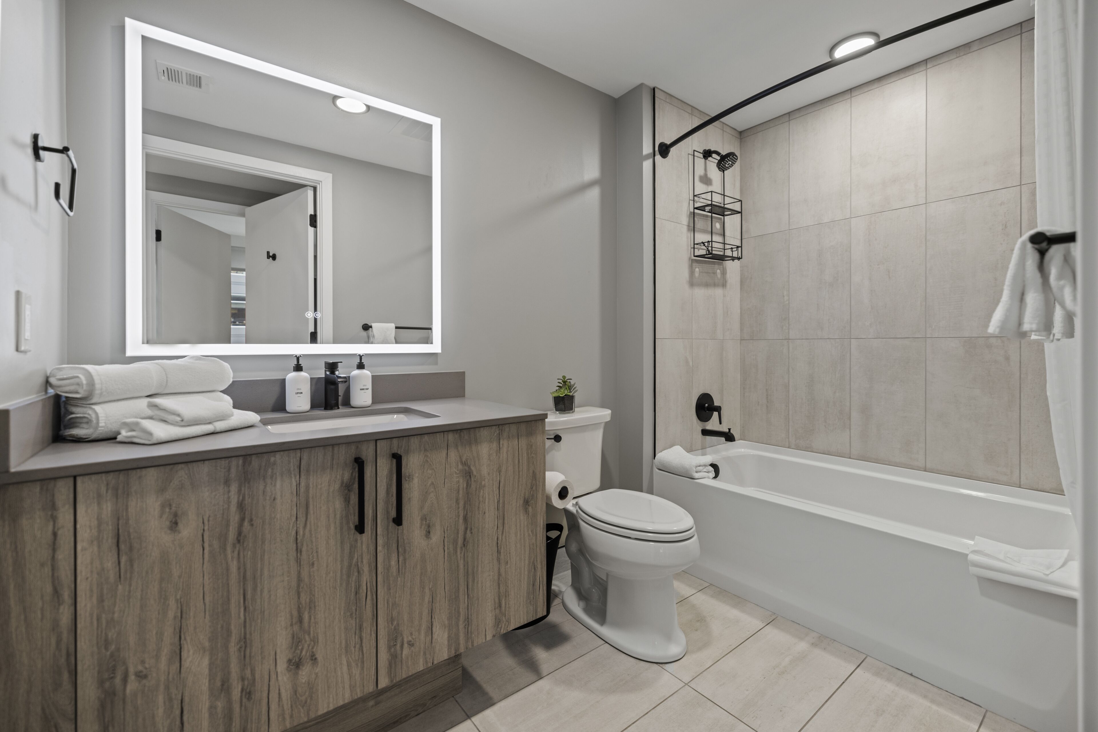 A modern bathroom with a wooden vanity, a large mirror, a toilet, and a walk-in shower.