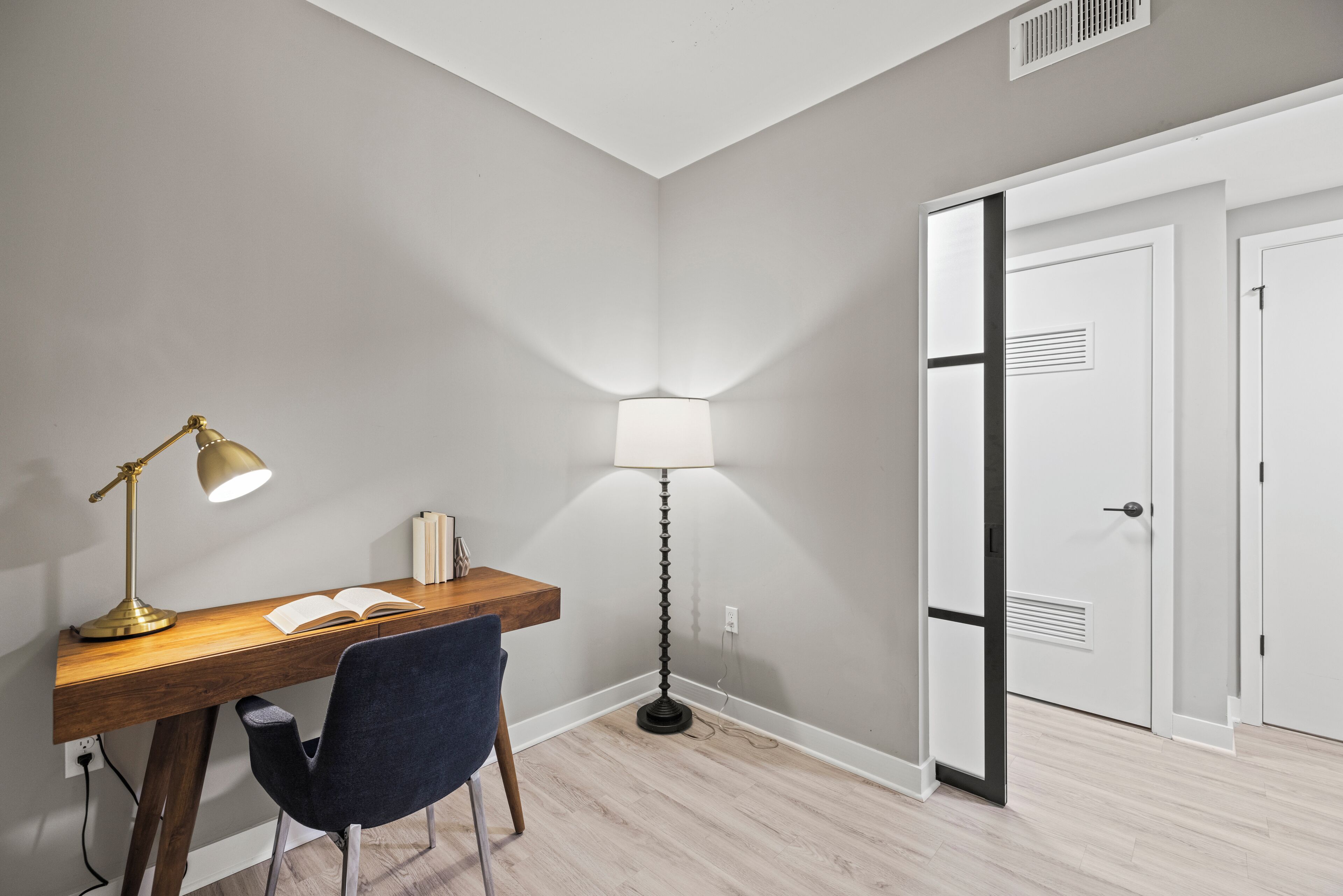 A study area with a desk, two lamps, a chair, and a door.