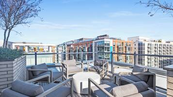 A rooftop terrace with outdoor seating, a view of modern buildings, and a clear sky.