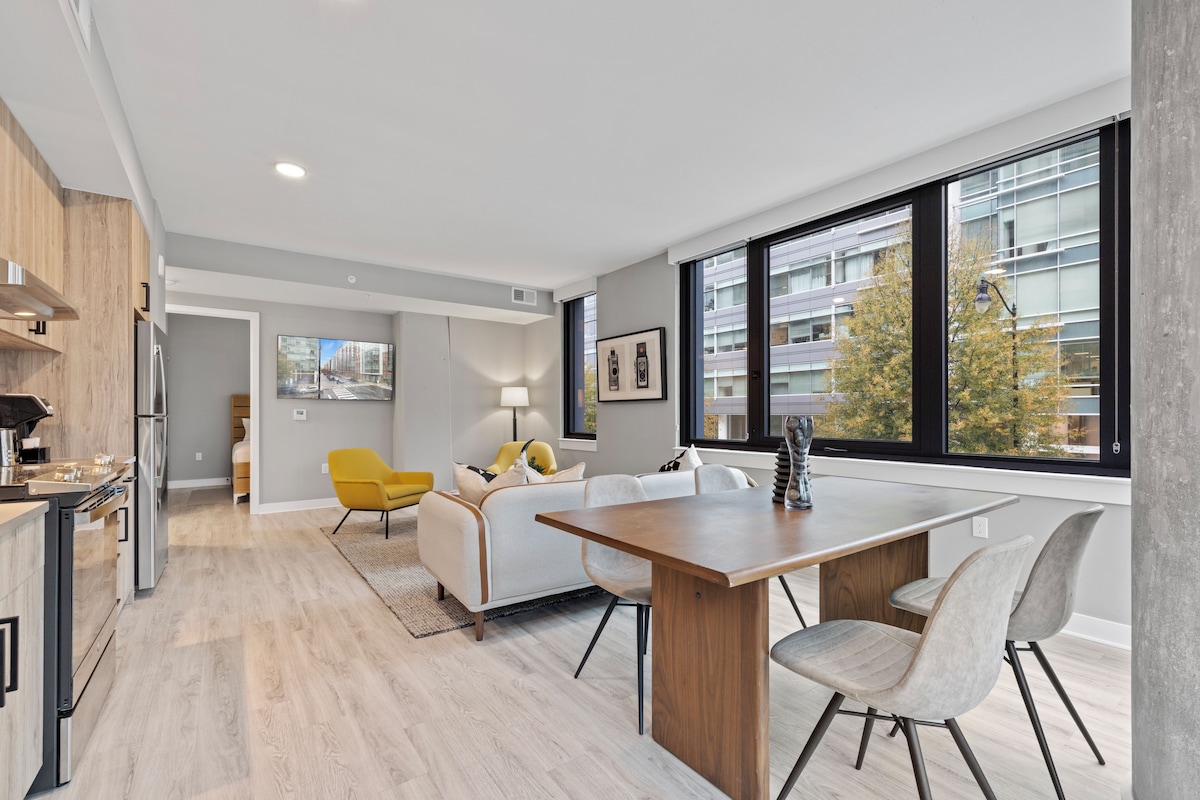 A modern kitchen with a dining area, a sofa, and a yellow chair.