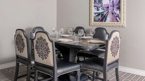 Een eettafel gedekt voor zes personen, met zwarte stoelen, een lijst met een foto aan de muur en een kamerbreed tapijt met een patroon.