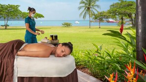 A person receiving a massage outdoors with a view of the sea and palm trees.