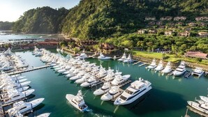 A marina with numerous boats docked, surrounded by lush greenery and residential buildings.