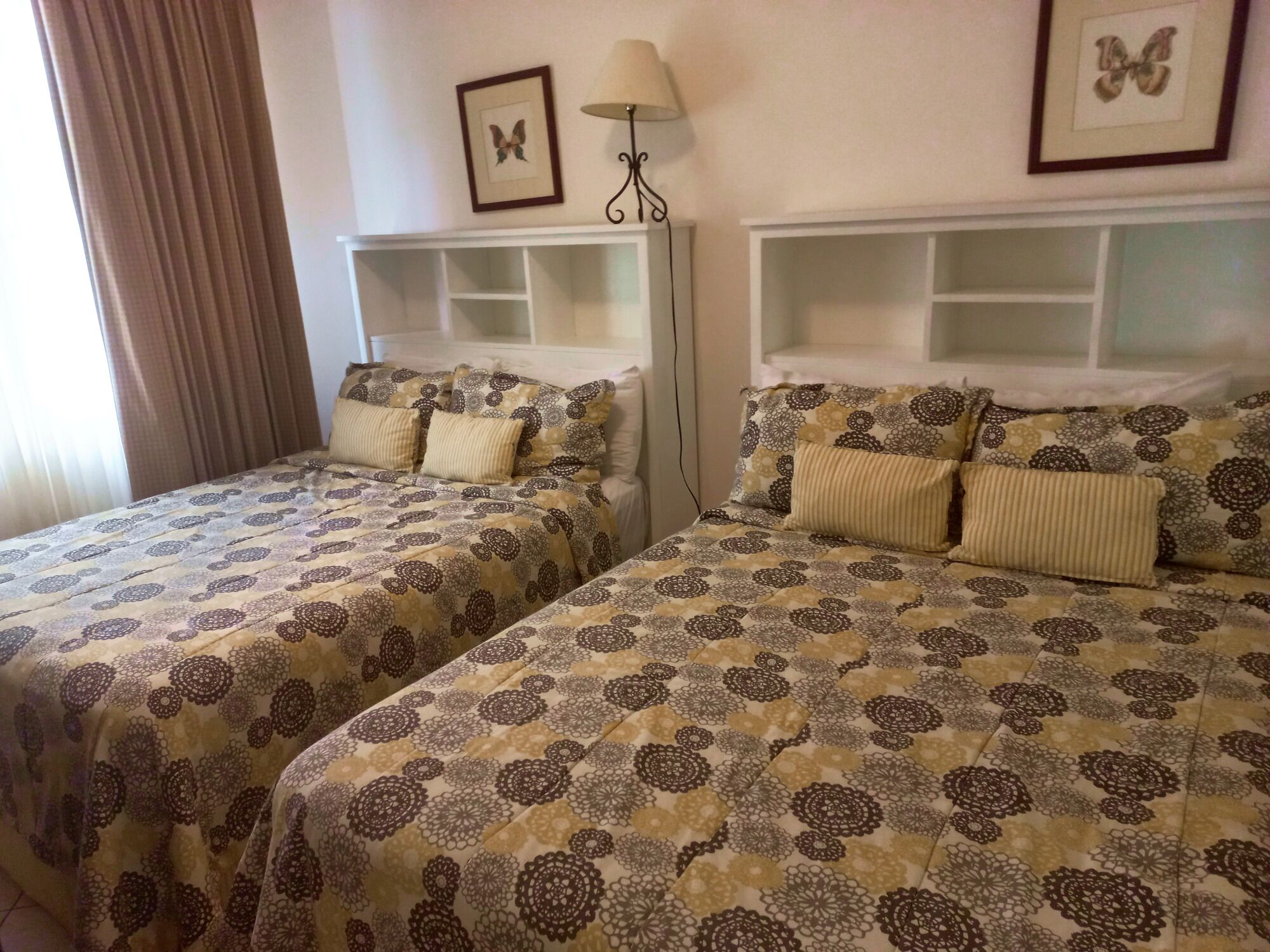Dos camas con ropa de cama estampada, una lámpara de noche y un cuadro de una mariposa en la pared.