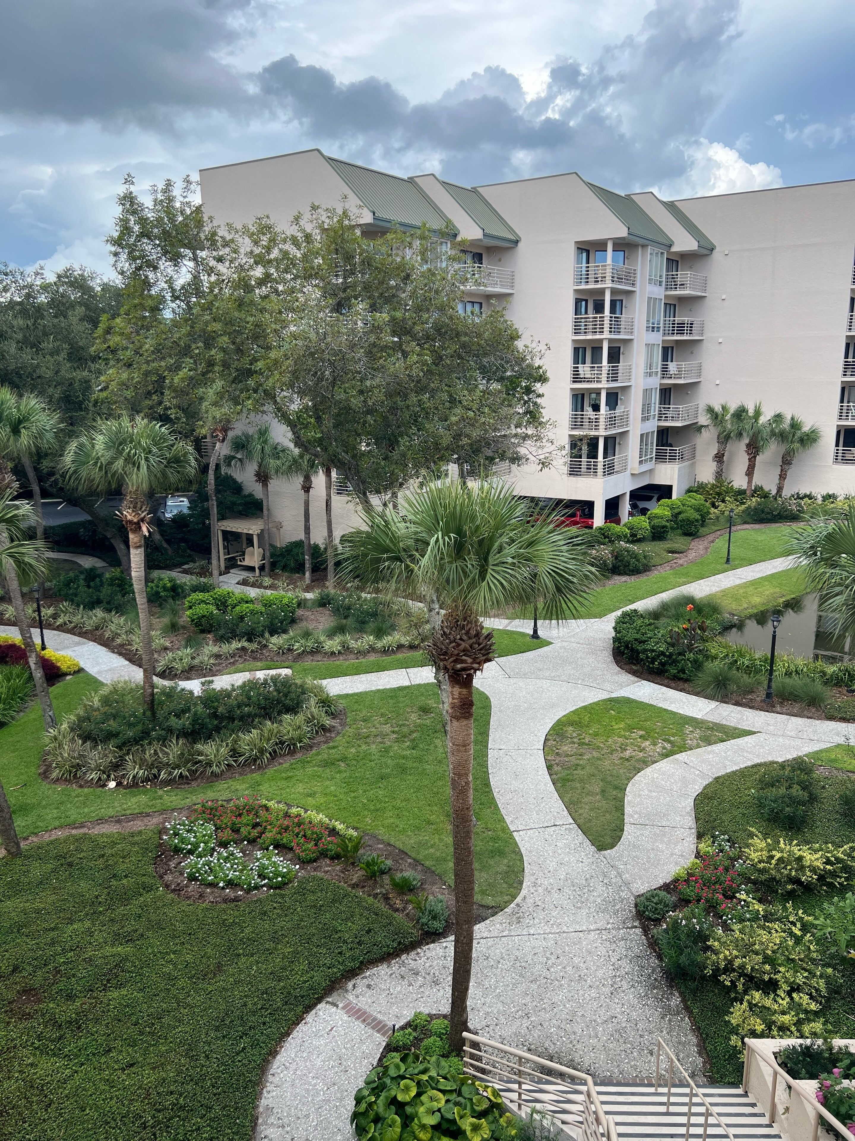 A modern hotel with a landscaped garden, a winding pathway, and a multi-story building with balconies.