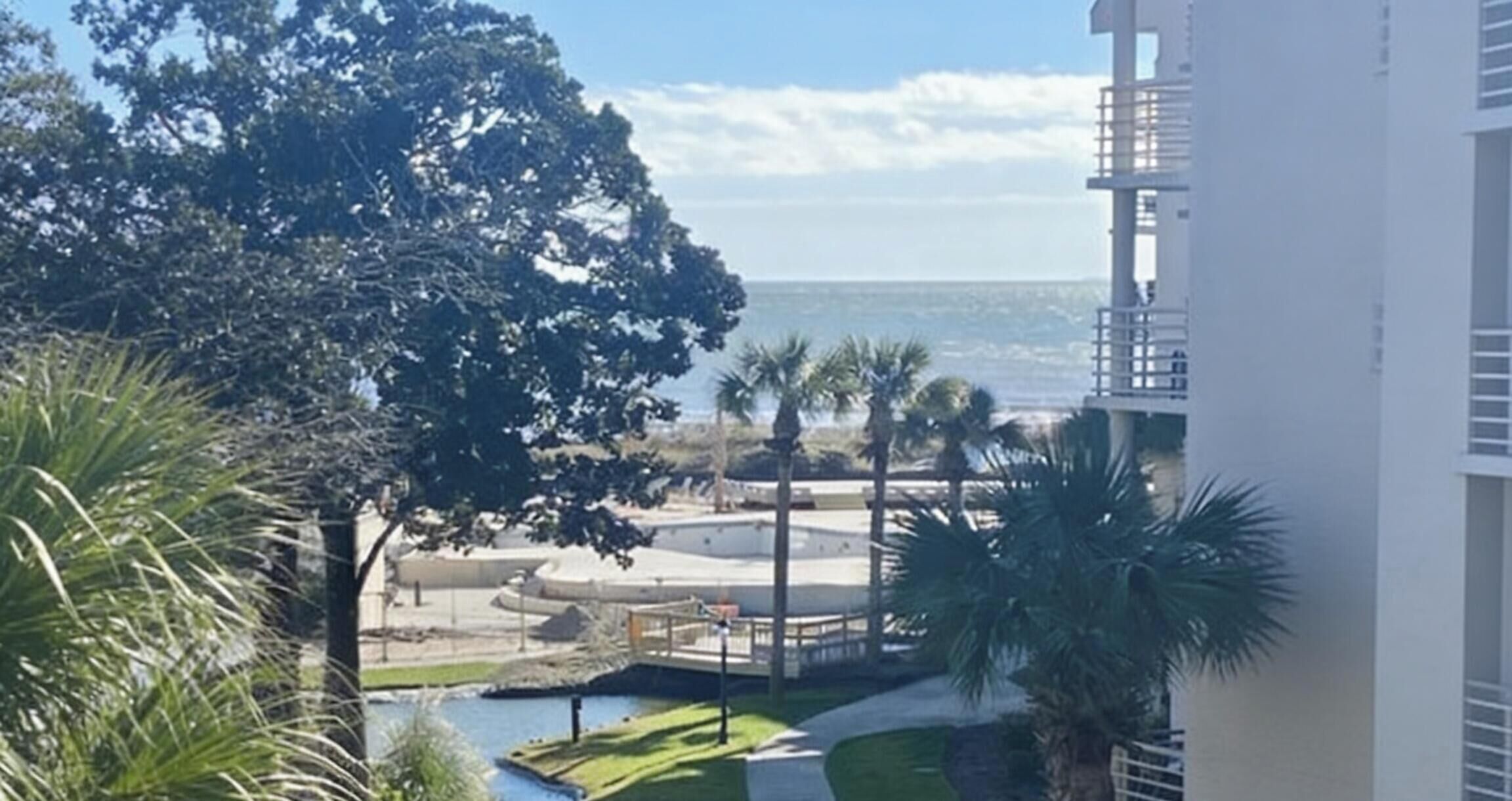 A view of a building with a pool, palm trees, and a clear sky.