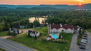 A large house with a swimming pool, surrounded by a lush green landscape and a lake. - Hôtel Matha (Saint-Jean-de-Matha)