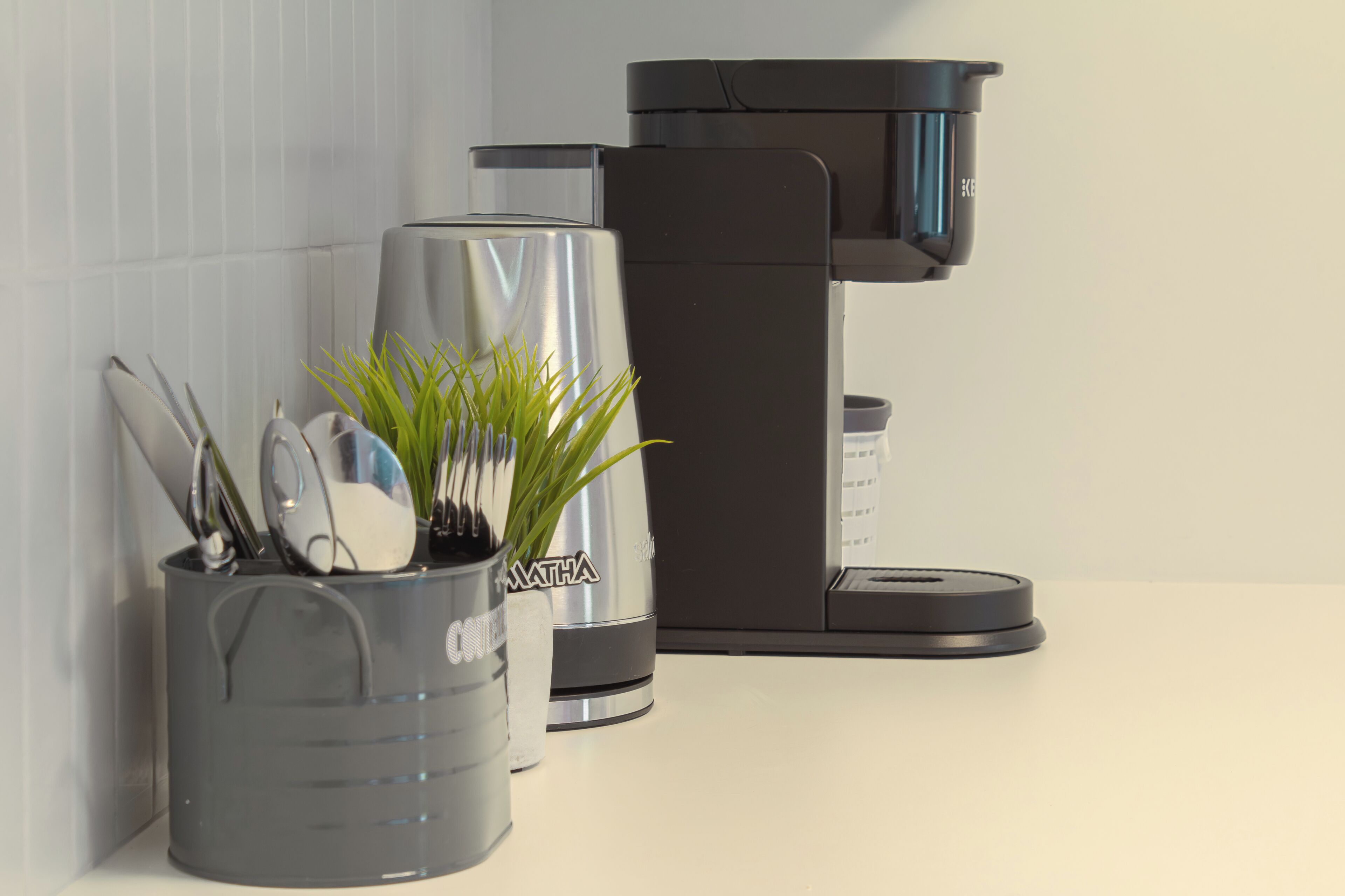 A kitchen with a coffee maker, a plant, and utensils.