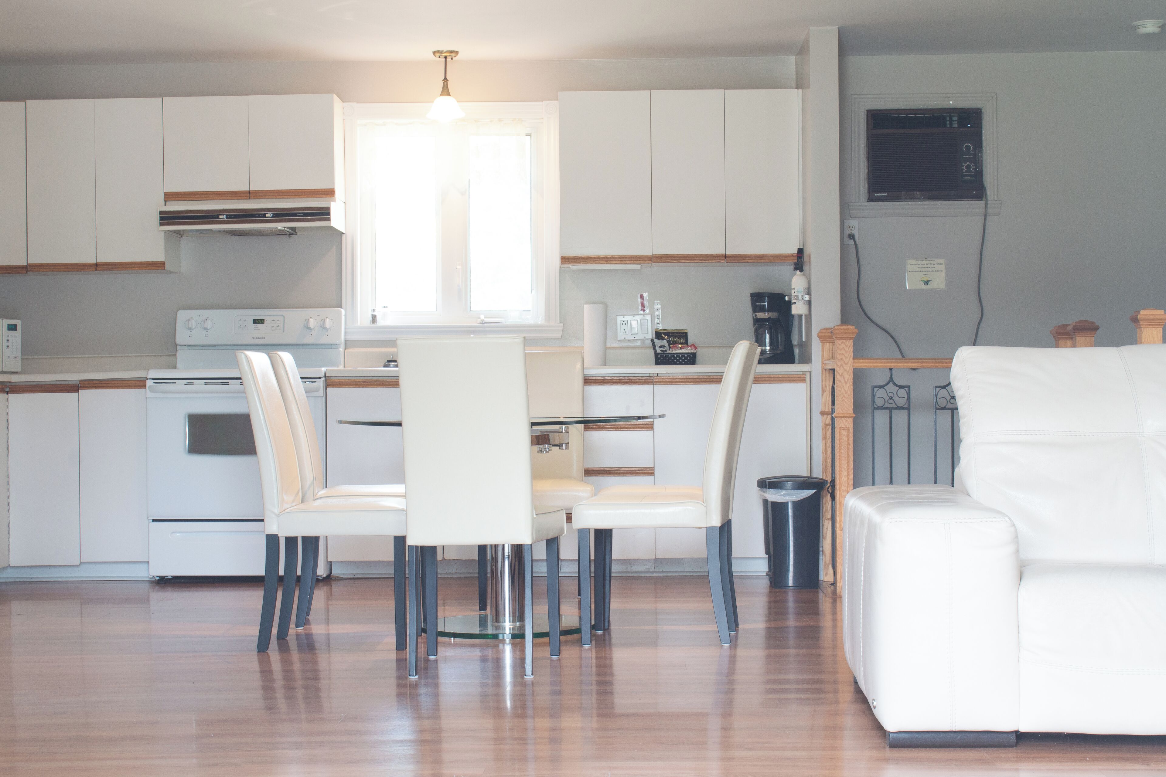 A modern kitchen with white cabinets, a dining area with white chairs, and a white sofa.