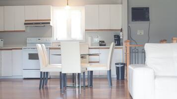 A modern kitchen with white cabinets, a dining area with white chairs, and a white sofa.