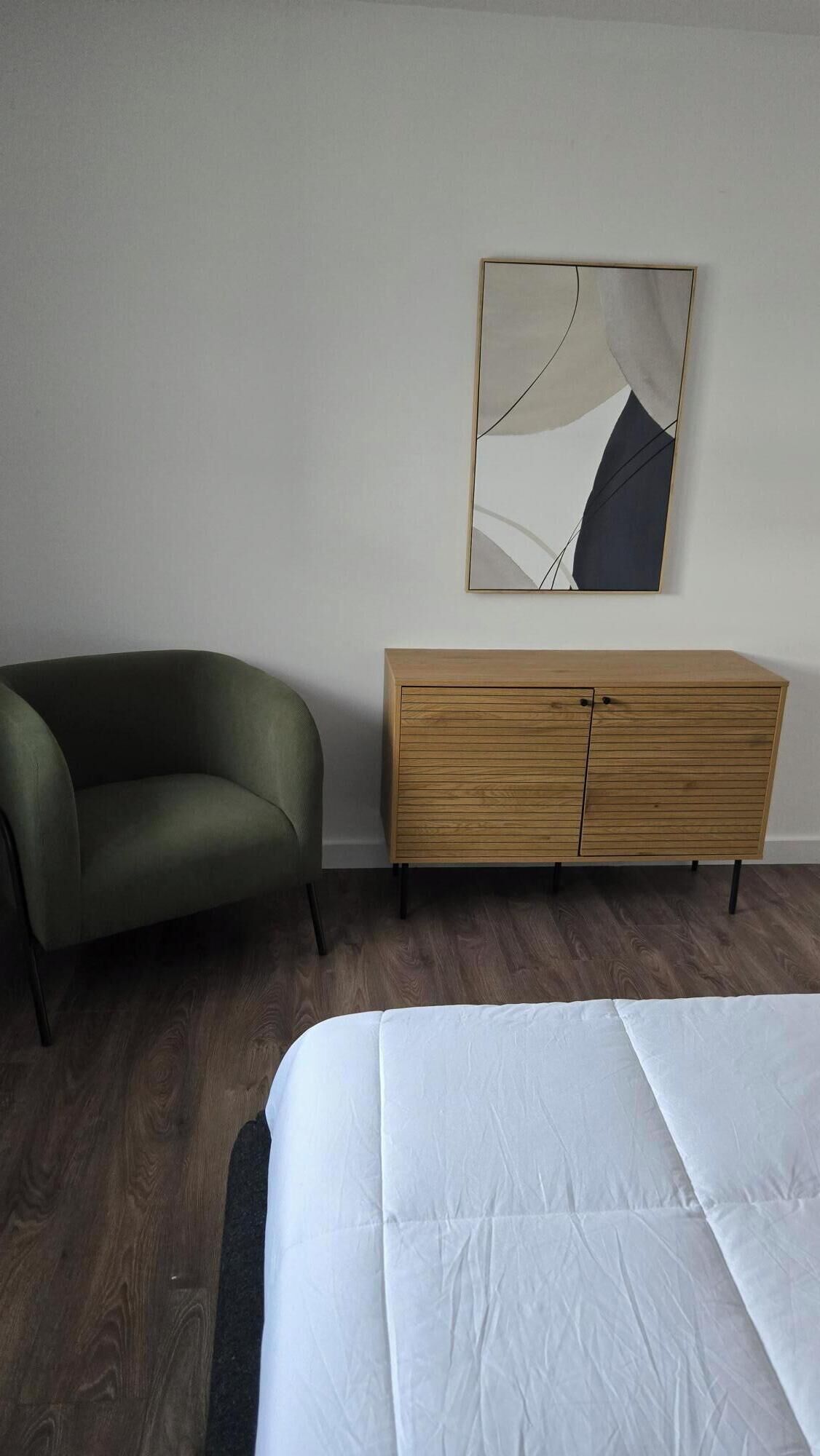 A hotel room with a green armchair, a wooden dresser, and a bed.
