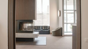 A modern living room with a fireplace, a sofa, and a large window. - Hôtel Matha (Saint-Jean-de-Matha)